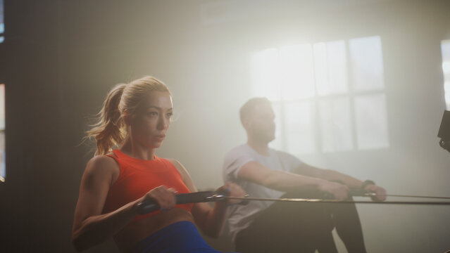Determined athletes training on rowing machine in gym