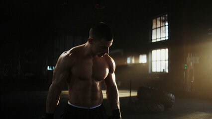 Muscular athlete preparing for intense workout in dark gym