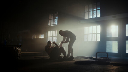 Determined male athletes training together doing sit-ups in dramatic gym