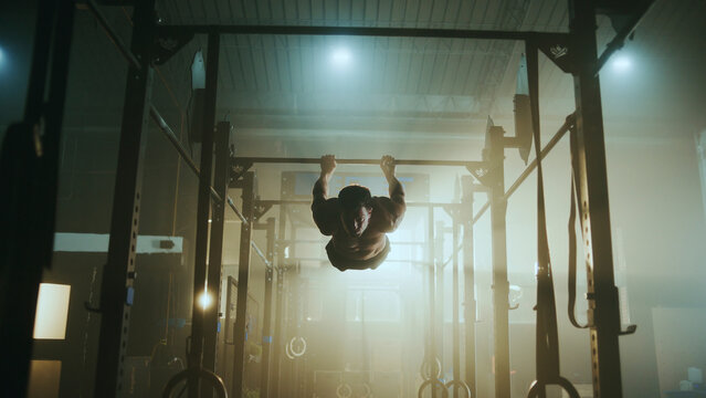 Determined male athlete performing hanging leg raises on pull-up bar in gym