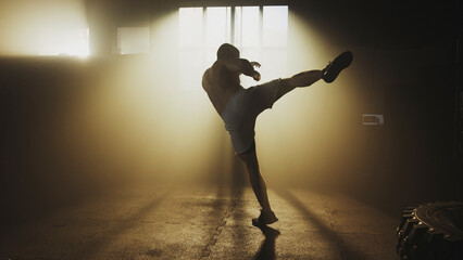 Muscular athlete performing a powerful high kick in a hazy gym