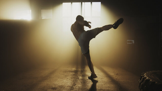 Muscular athlete performing a powerful high kick in a hazy gym