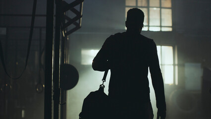 Athlete leaving gym after evening workout in dark interior