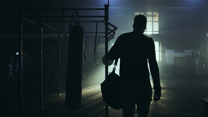 Boxer entering boxing gym with sports bag at night