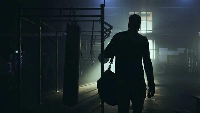 Boxer entering boxing gym with sports bag at night