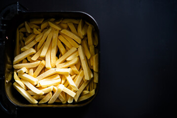 Golden french fries in air fryer basket on black background.