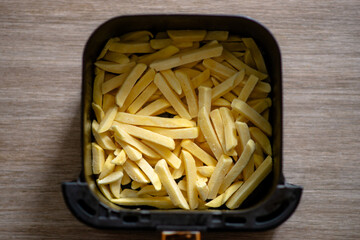 Uncooked frozen french fries in air fryer on wooden surface.