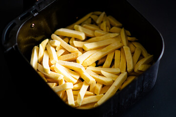 Frozen french fries cooking in air fryer close-up on dark background.