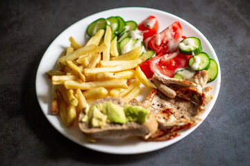 Healthy plate with fries, chicken, fresh vegetables, and avocado on bread.
