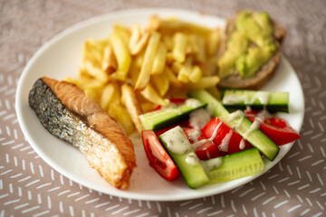 Healthy meal with grilled salmon, fresh vegetables, and fries on a plate.