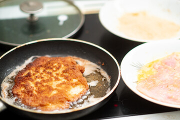 Crispy breaded cutlet frying on skillet with raw ingredients nearby.