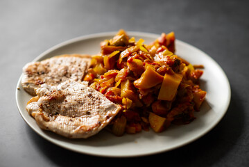 Grilled chicken with vegetable ratatouille on white plate.