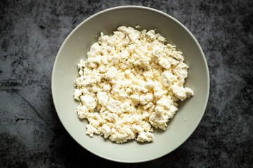 Fresh homemade ricotta cheese in white bowl on dark background.