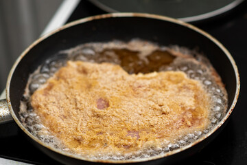 Breaded schnitzel frying in pan with bubbling oil on stove.