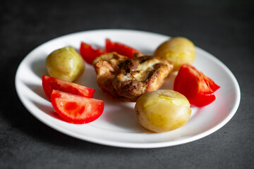 Chicken with boiled potatoes and fresh tomato on white plate.