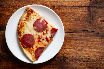 Pepperoni pizza slice on white plate with wooden table background.