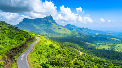 Fototapeta premium Scenic mountain landscape featuring winding road through lush green hills under bright blue sky with fluffy clouds
