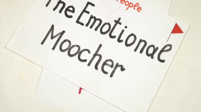 Sheets of paper with words 'The Emotional Moocher", "The Strait Jacket&raquo; handwritten on them are being laying out on a table. Visual aids on the topic "Toxic people"