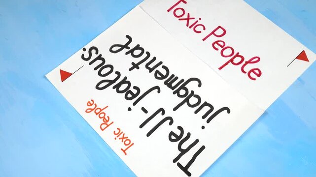 Words &ldquo;The JJ - a jealous-judgmental&rdquo;   handwritten on a white sheet of paper. Sheets of paper with written theses on the topic &laquo;Toxic People&raquo; are on a blue background 