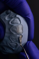 Dental resin application on tooth model with dental tool in gloved hand close-up
