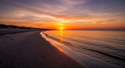 Naklejka premium Seaside sunset; sand beach with colorful sky reflecting on calm water