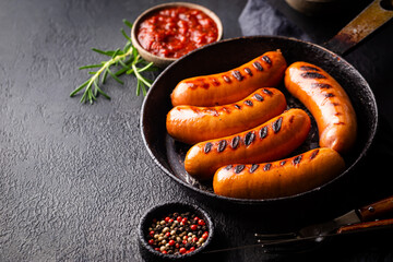 Fried delicious sausages with tomato sauce and herbs in a pan, black background.