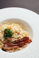 Creamy Pasta with Crispy Bacon and Mixed Vegetables on White Plate