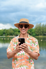 Hispanic Male Tourist in Panama Hat and Tropical Shirt Using Smartphone at Beach