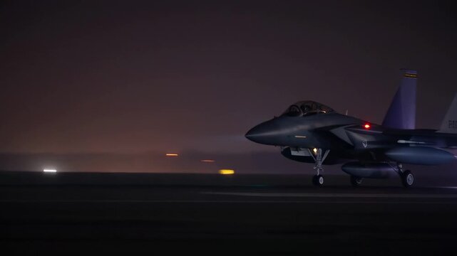 Fighter jet taxiing on runway at night with afterburners active