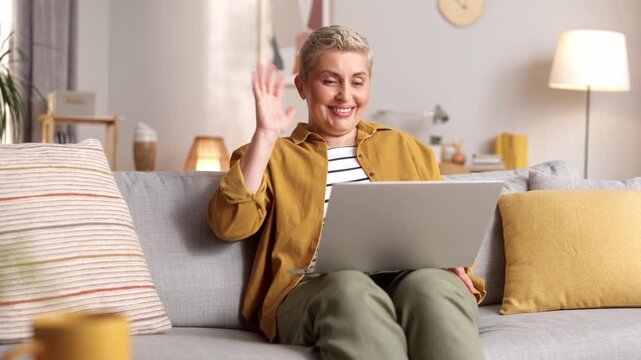 Positive smiling lady talking using laptop computer enjoying online virtual chat video call with friends or family in distance e chat virtual meeting using pad computer sitting on sofa at home.
