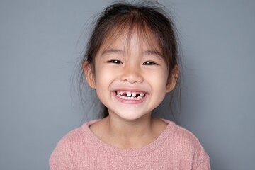 Smiling young Asian girl with chipped teeth isolated on grey background