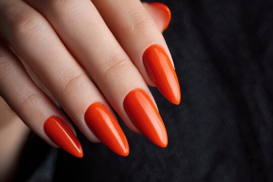 Woman s hand with elongated nails and vibrant red orange polish