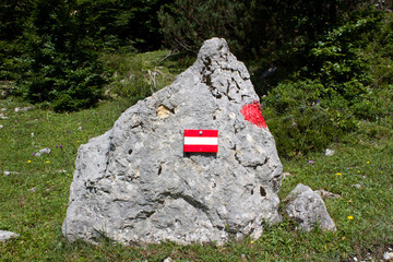 Red and white striped markings on a large rock in a mountainous area during a sunny day surrounded...