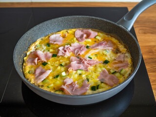 Frittata - scrambled eggs with zucchini and boiled ham in frying pan