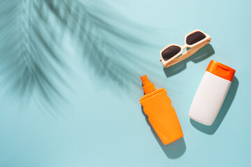 Sunscreen, sunglasses and seashell on blue background with hard sunny shadows.