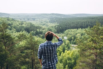 Young man gazing at scenic forest from behind on a summer day embracing outdoor adventure