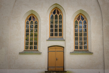 Obraz premium Facade of a church with three tall arched windows and a central wooden door in warm yellow tones.
