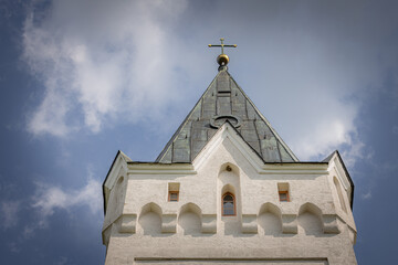Close-up of a white church tower with a green roof and golden cross against a blue sky with...
