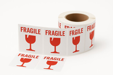 Close-up of fragile label stickers on a roll, red glass icon for parcel protection and handling instructions on white background