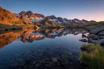 Scenic alpine lake reflecting snow-capped mountain peaks at sunrise with clear sky and rocky shoreline, tranquil nature landscape photography concept

