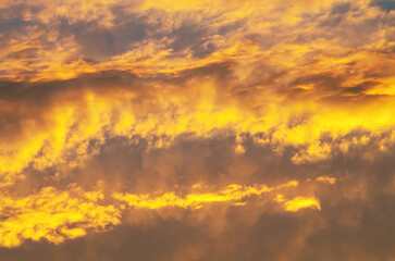 Golden sunset sky with radiant orange clouds and dark gray streaks creating a glowing horizon scene