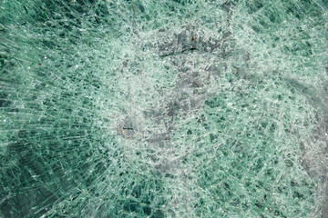 A closeup view of a broken car windshield. The window is completely destroyed.