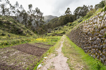 Ancient Inca stone terraces at the archaeological site of Chinchero, Peru against misty Andean...