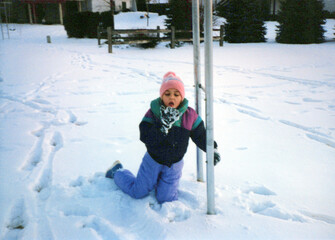 Child in the 80s, playing in the snow, eating snow, wearing a snowsuit. Vintage scan, may have imperfections
