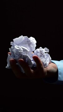 Crumpled paper balls on a black background in the hands of a man.
A businessman in a blue shirt holds in his hands an unnecessary crumpled paper that he is going to throw away.
Trash in the office