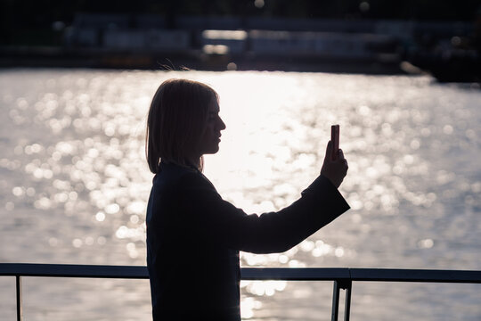 Young woman taking a smartphone selfie by the water during sunset - Powered by Adobe