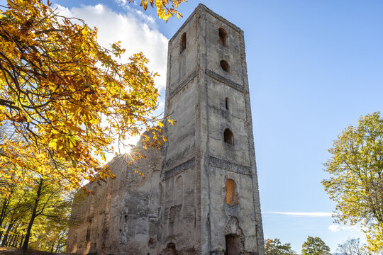 The Katarinka, ruins of a Franciscan monastery and church in Slovakia, Europe. Towering stone structure stands amidst trees, sun shining through autumnal foliage against the bright sky.