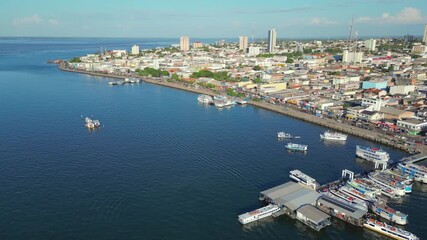 Aerial drone video of Santarem, Para, Brazil, located on the banks of the Tapajos river, showing boats docked at piers along the waterfront and the city’s historic and commercial center