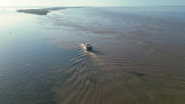 Aerial drone video of a ferryboat transporting vehicles and passengers across the meeting of the waters of the Amazon river (right) and Tapajos river (left) in Santarem, Para, Brazil