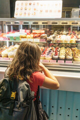 Back shot of a child girl with backpack admiring cupcakes in bakery window display